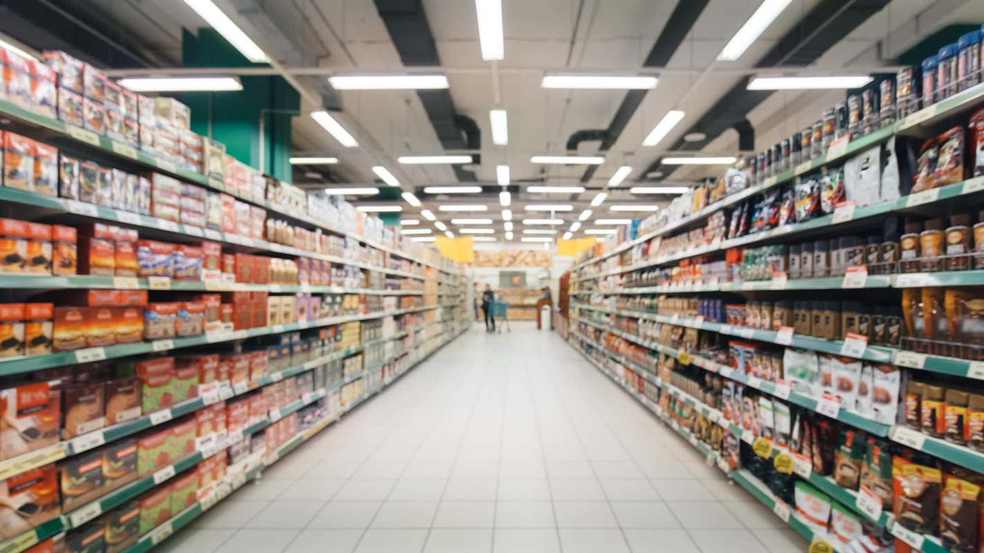 A grocery store aisle lined with various packaged food products and a shopping cart in the distance.