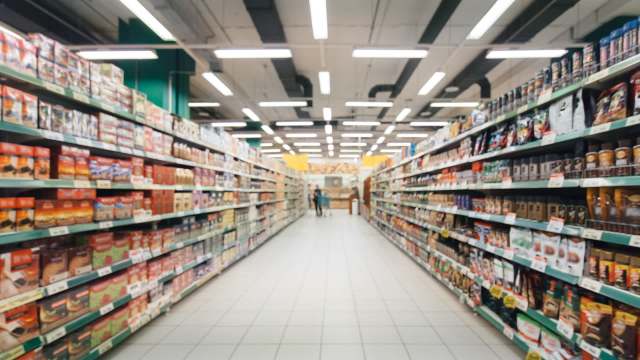 A grocery store aisle lined with various packaged food products and a shopping cart in the distance.