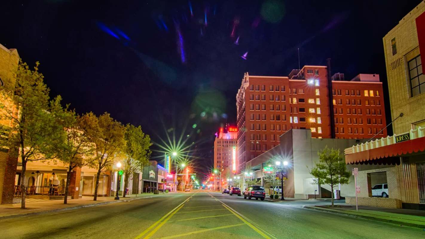 A city street at night lined with buildings, streetlights, and illuminated signs.