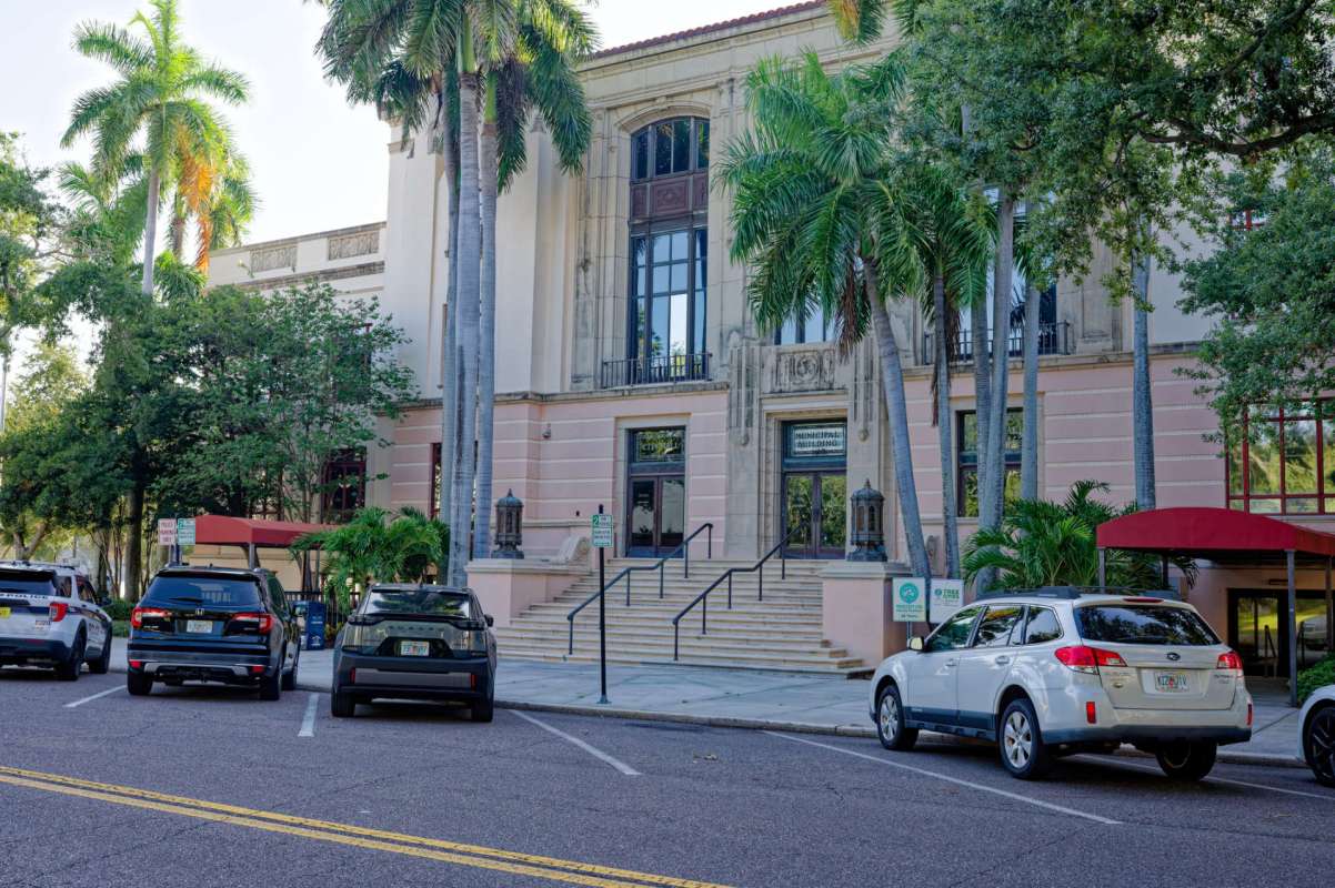A historic building with palm trees and parked cars in front.