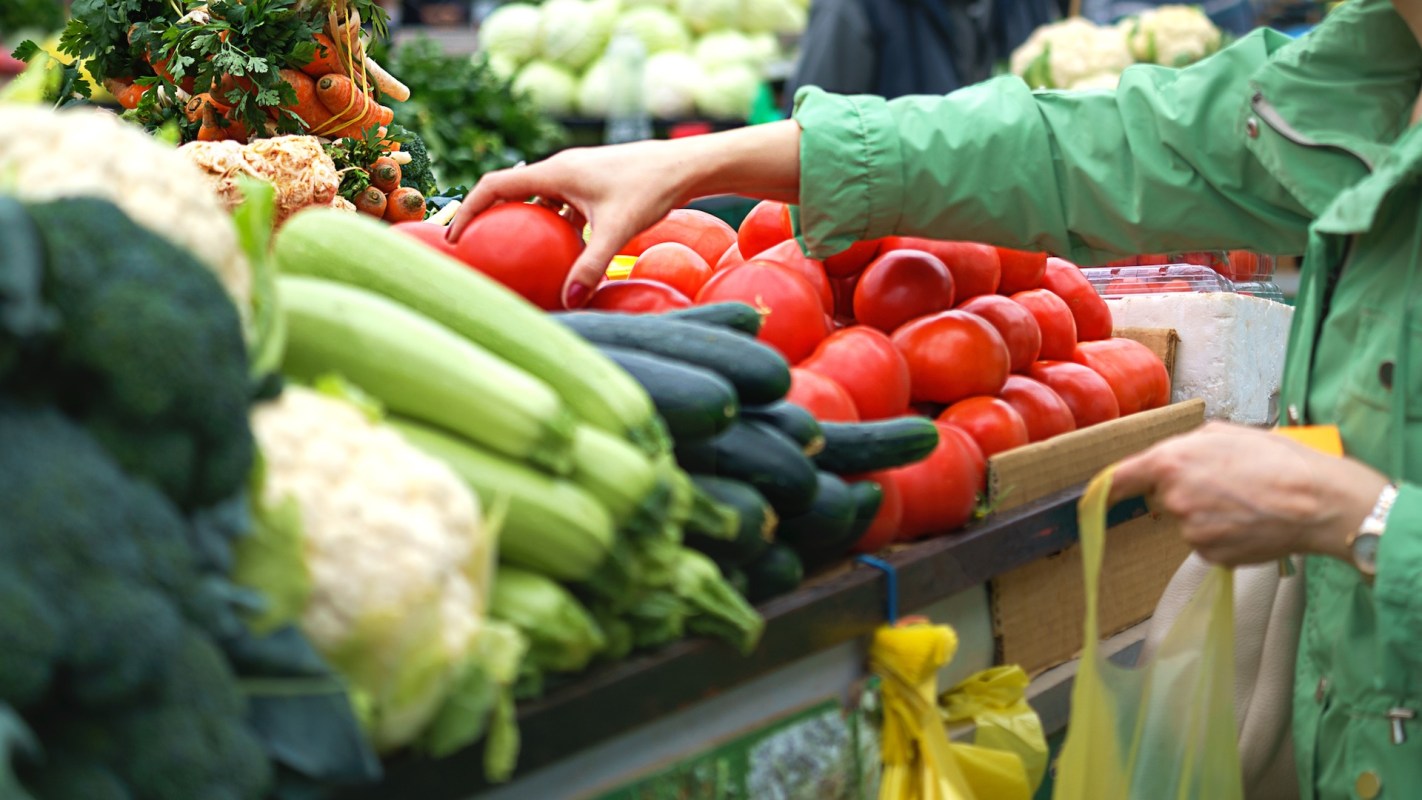 A person selects tomatoes from a display of fresh vegetables at a market.
