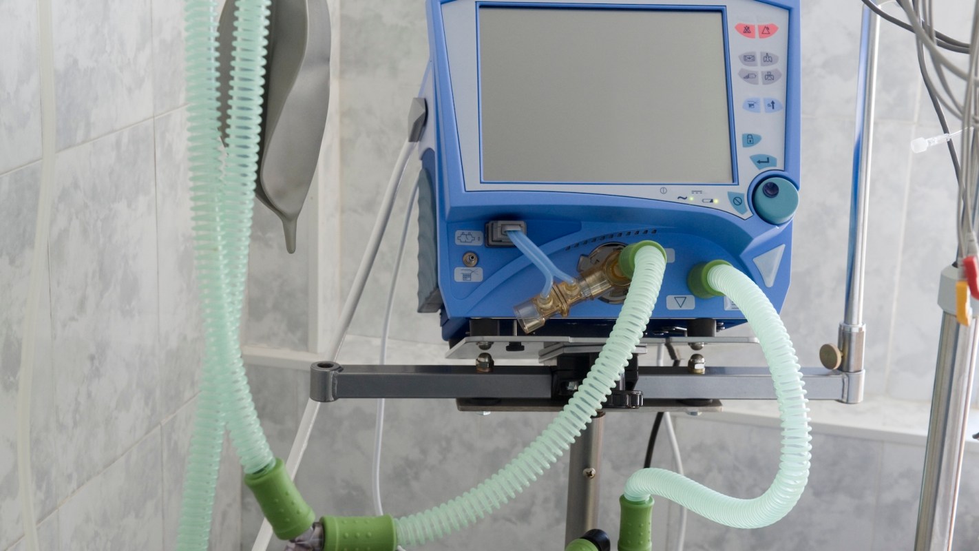 A medical ventilator with connected tubes in a clinical environment.