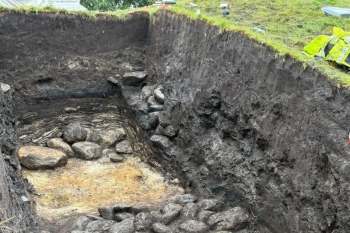 An excavated trench revealing layers of soil and stones.