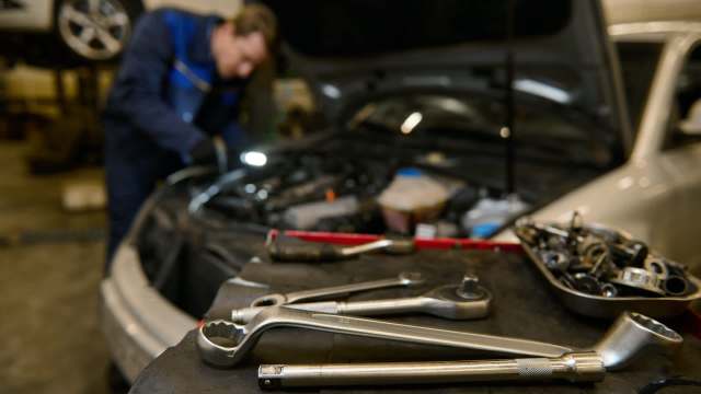 A mechanic works on a car engine while various tools are arranged on a table in the foreground.