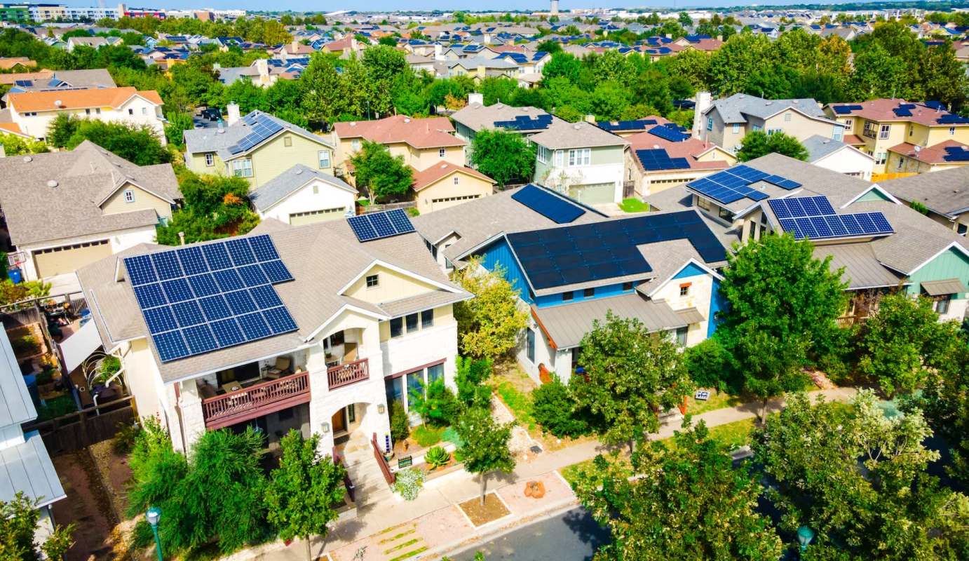 Aerial view of houses with solar panels and greenery in a suburban neighborhood.
