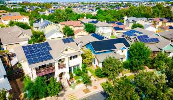 Aerial view of houses with solar panels and greenery in a suburban neighborhood.