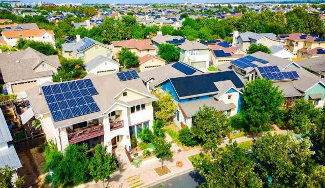 Aerial view of houses with solar panels and greenery in a suburban neighborhood.
