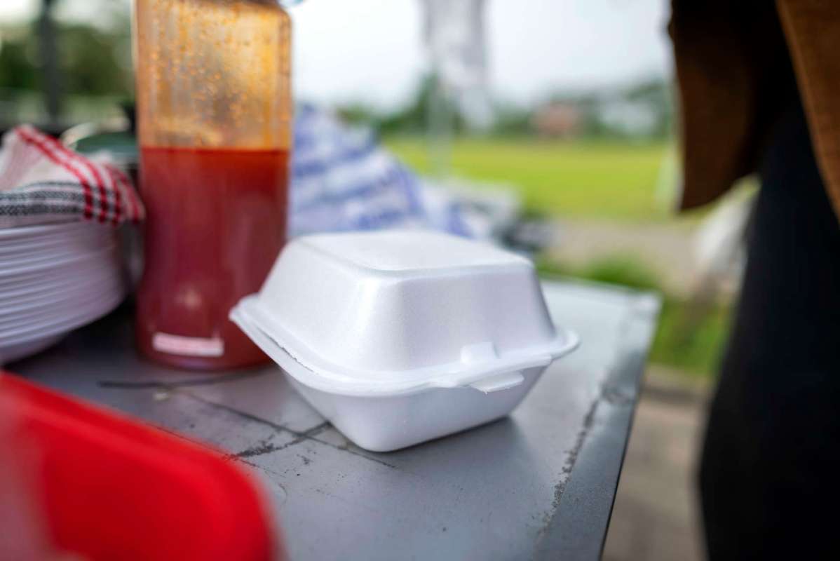 A takeout container on a table next to a bottle of sauce and stacked plates.