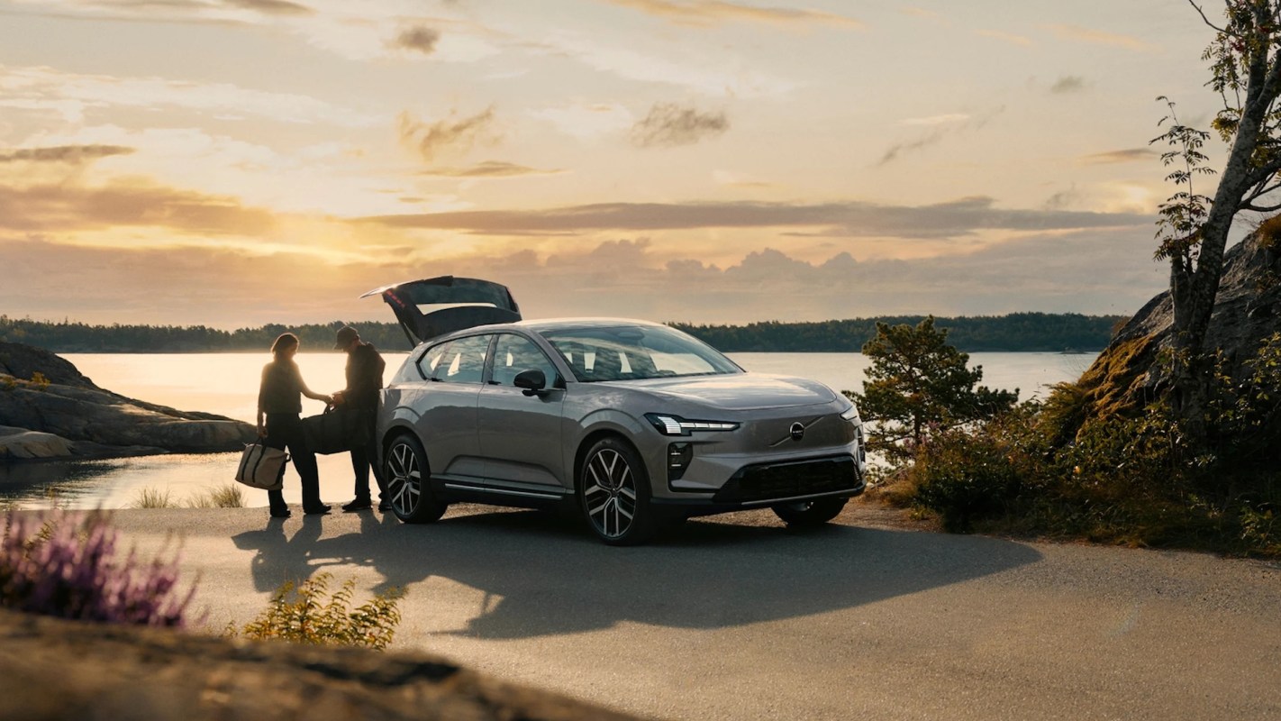 Two people unpacking bags from a car by a lake.