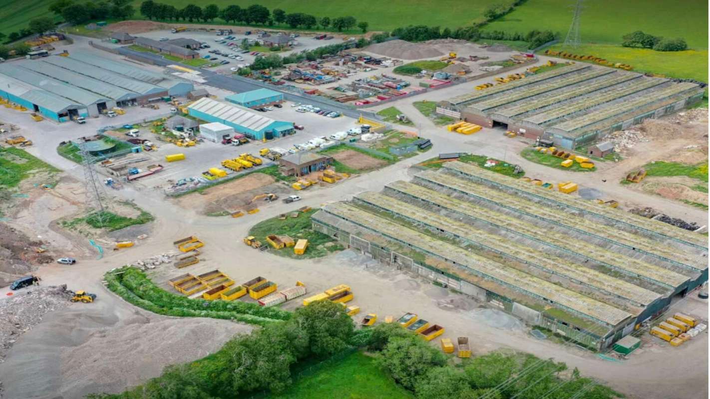 An aerial view of an industrial site with storage buildings, construction materials, and parked vehicles.