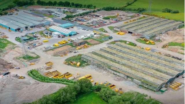 An aerial view of an industrial site with storage buildings, construction materials, and parked vehicles.