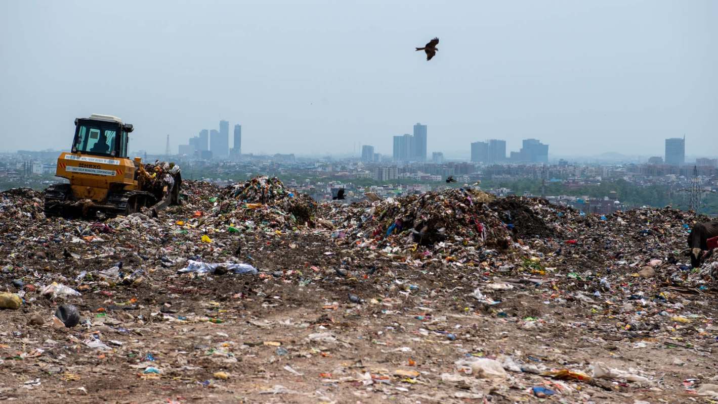 A bulldozer operates in a large landfill with a city skyline in the background.