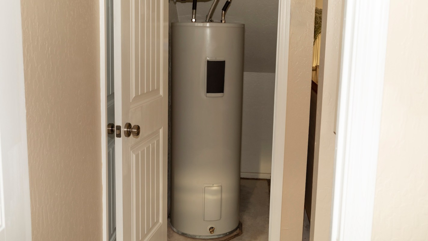 A water heater installed in a small closet space with white doors.