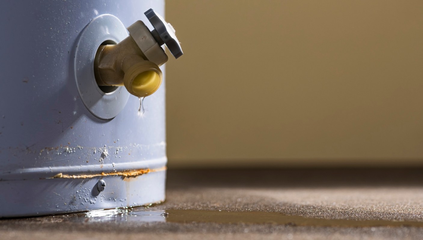 A leaking valve attached to a water tank, with water pooling on the floor beneath it.