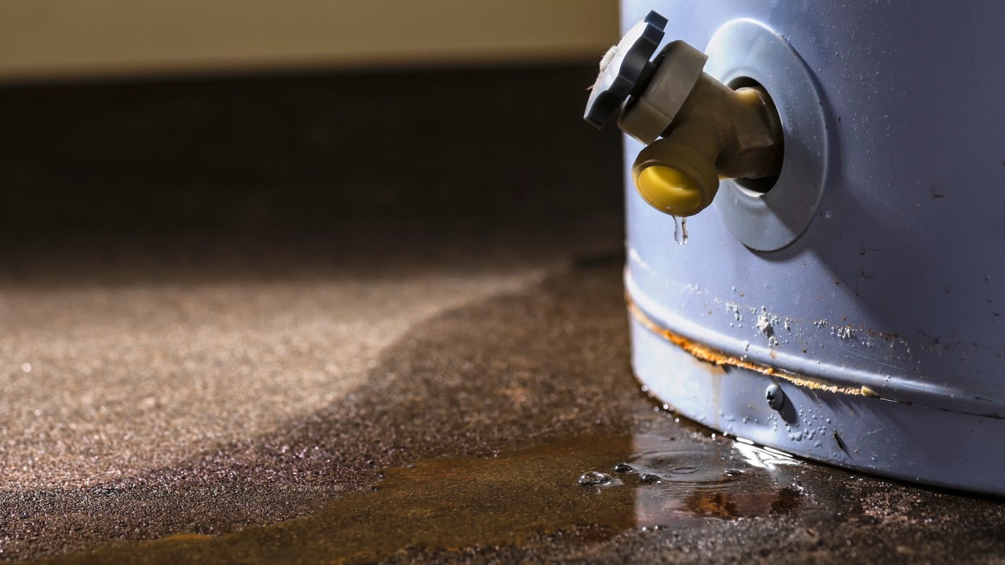 A leaking valve on a water tank with water pooling on the floor.