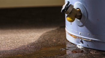 A leaking valve on a water tank with water pooling on the floor.