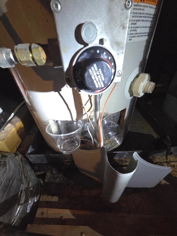 A water heater with connected pipes and a drain pan on a concrete floor.