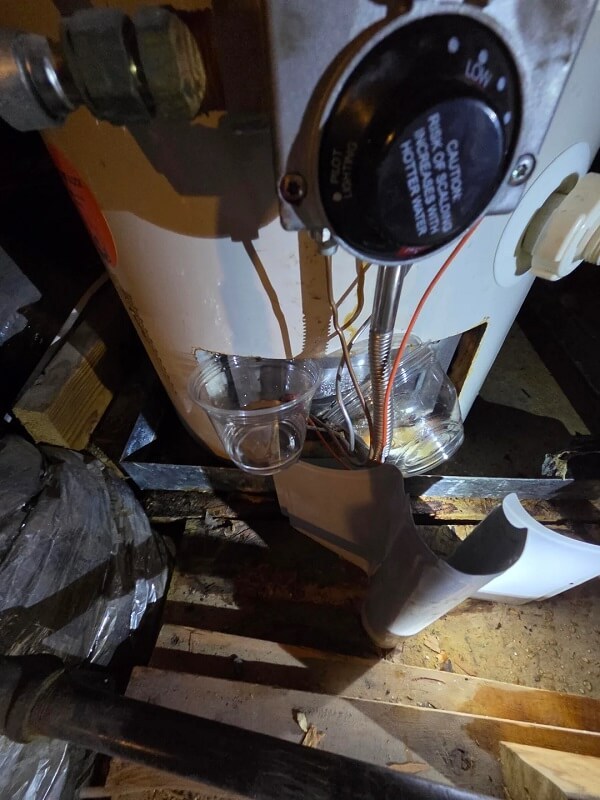 A water heater with connected pipes and a drain pan on a concrete floor.