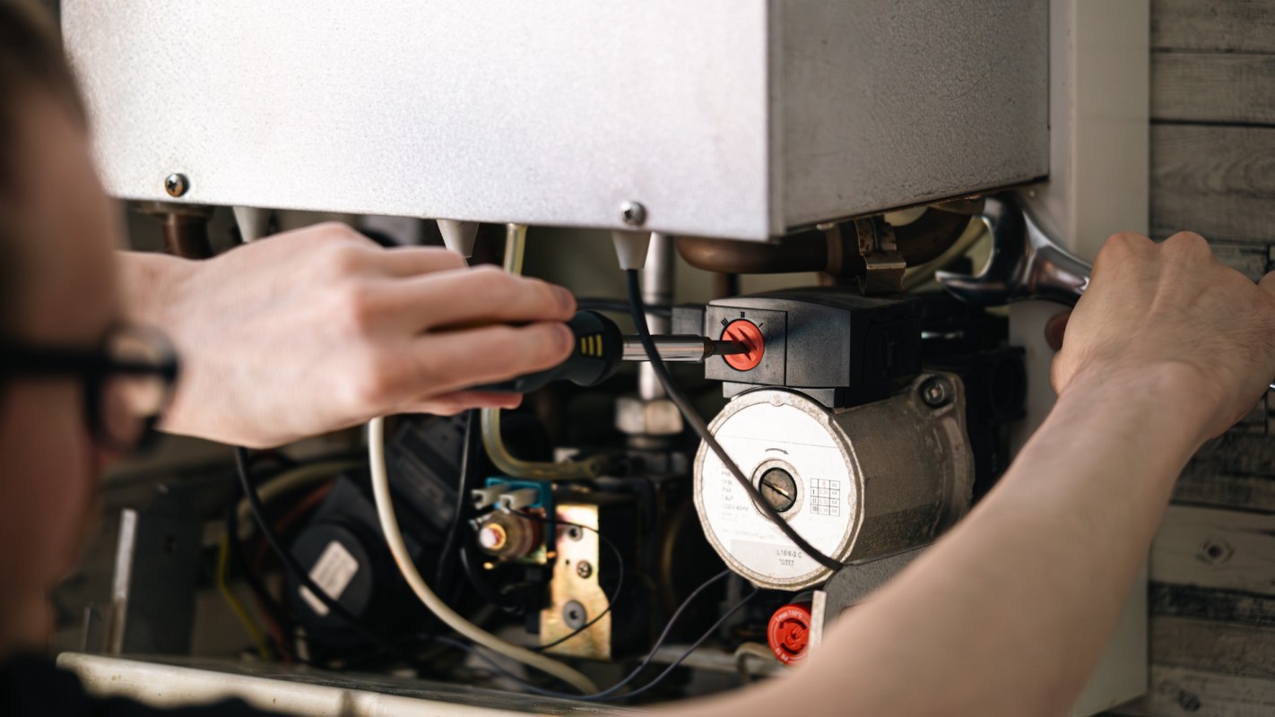 A person uses a screwdriver to work on a mechanical device with visible wires and components.