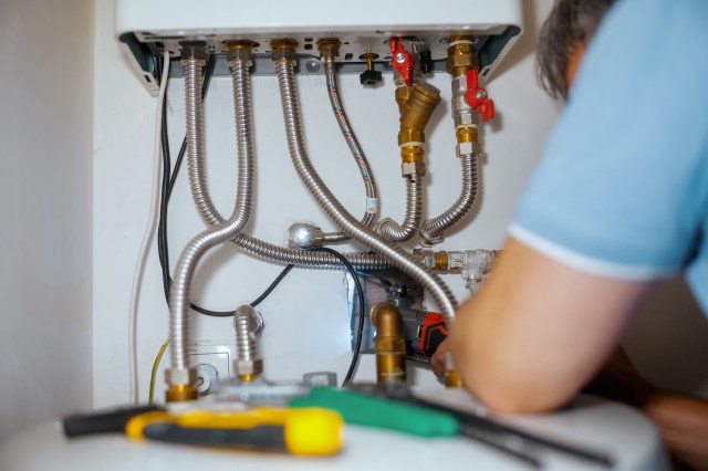 A person works on plumbing connections near a water heater with various pipes and fittings.