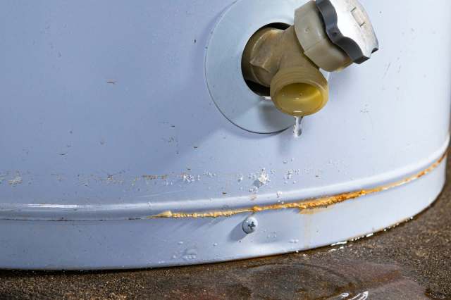 A leaking valve on a gray cylindrical container with water pooling beneath it.