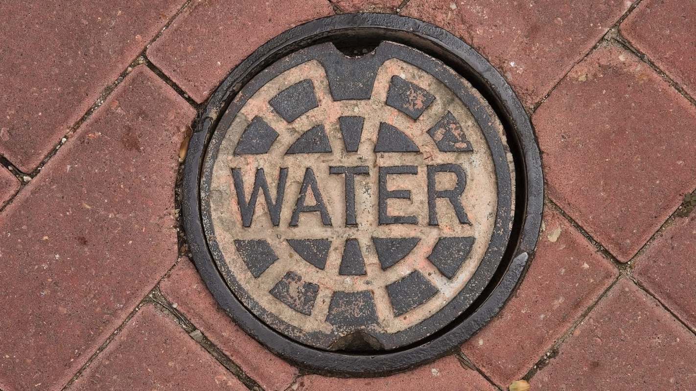 A manhole cover labeled "WATER" on a brick pavement.