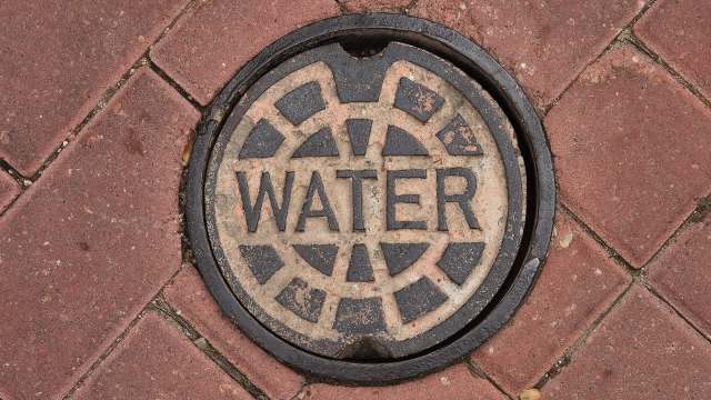 A manhole cover labeled "WATER" on a brick pavement.