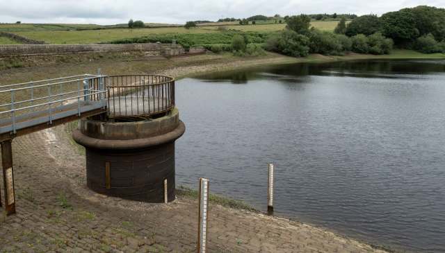 A water inlet structure beside a calm reservoir with surrounding greenery and stone banks.