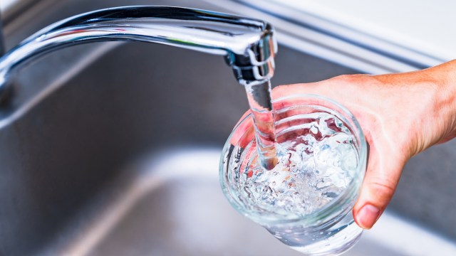 A hand pouring water from a faucet into a glass.