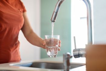 A person filling a water glass at the sink.
