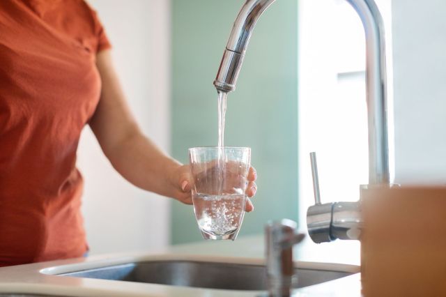 A person filling a water glass at the sink.