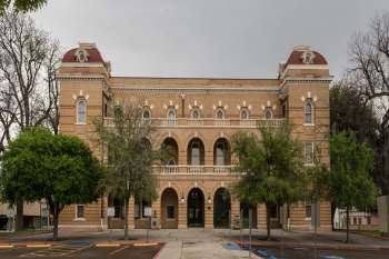 A historic brick building with arched entrances and trees in front.