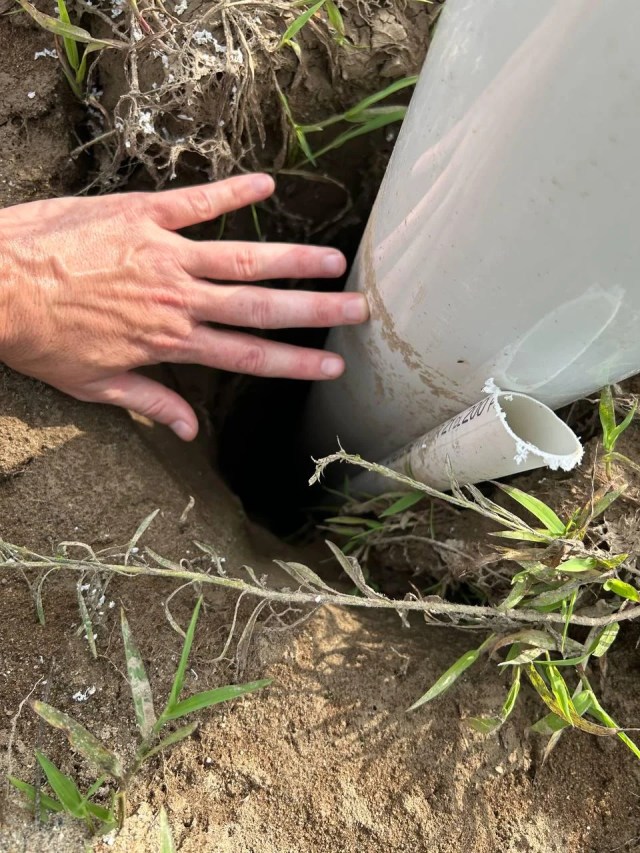 A person wiggling a water pipe in a hole.