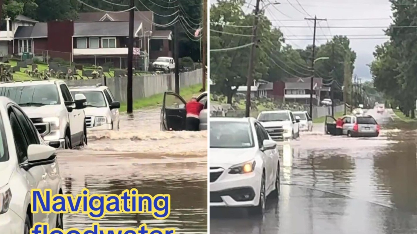 Cars navigate through a flooded street with water levels rising.