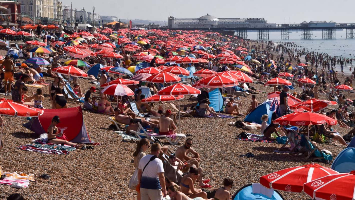 A crowded beach with numerous people under colorful umbrellas and tents.