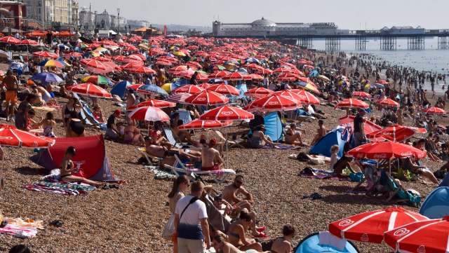 A crowded beach with numerous people under colorful umbrellas and tents.