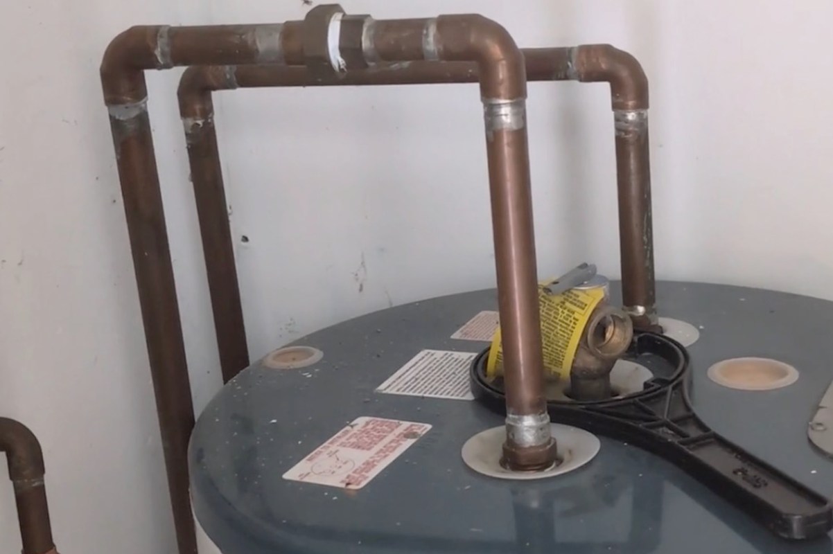 A water heater with copper piping and a wrench on top.