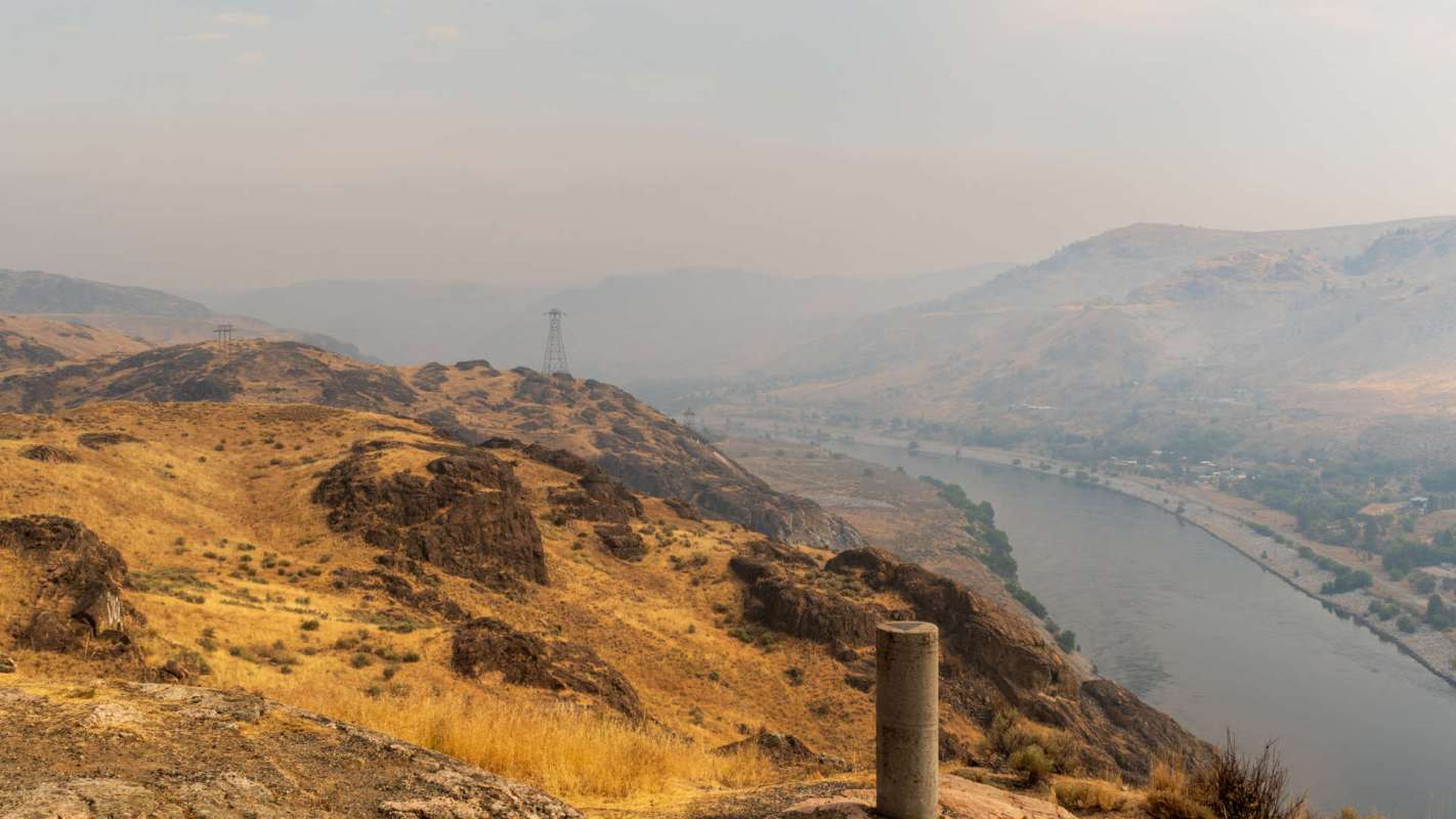 A view of a river winding through dry, rocky terrain under a hazy sky.