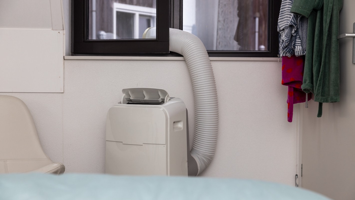 A portable air conditioner with a vent hose next to hanging clothes in a room.