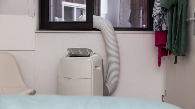 A portable air conditioner with a vent hose next to hanging clothes in a room.