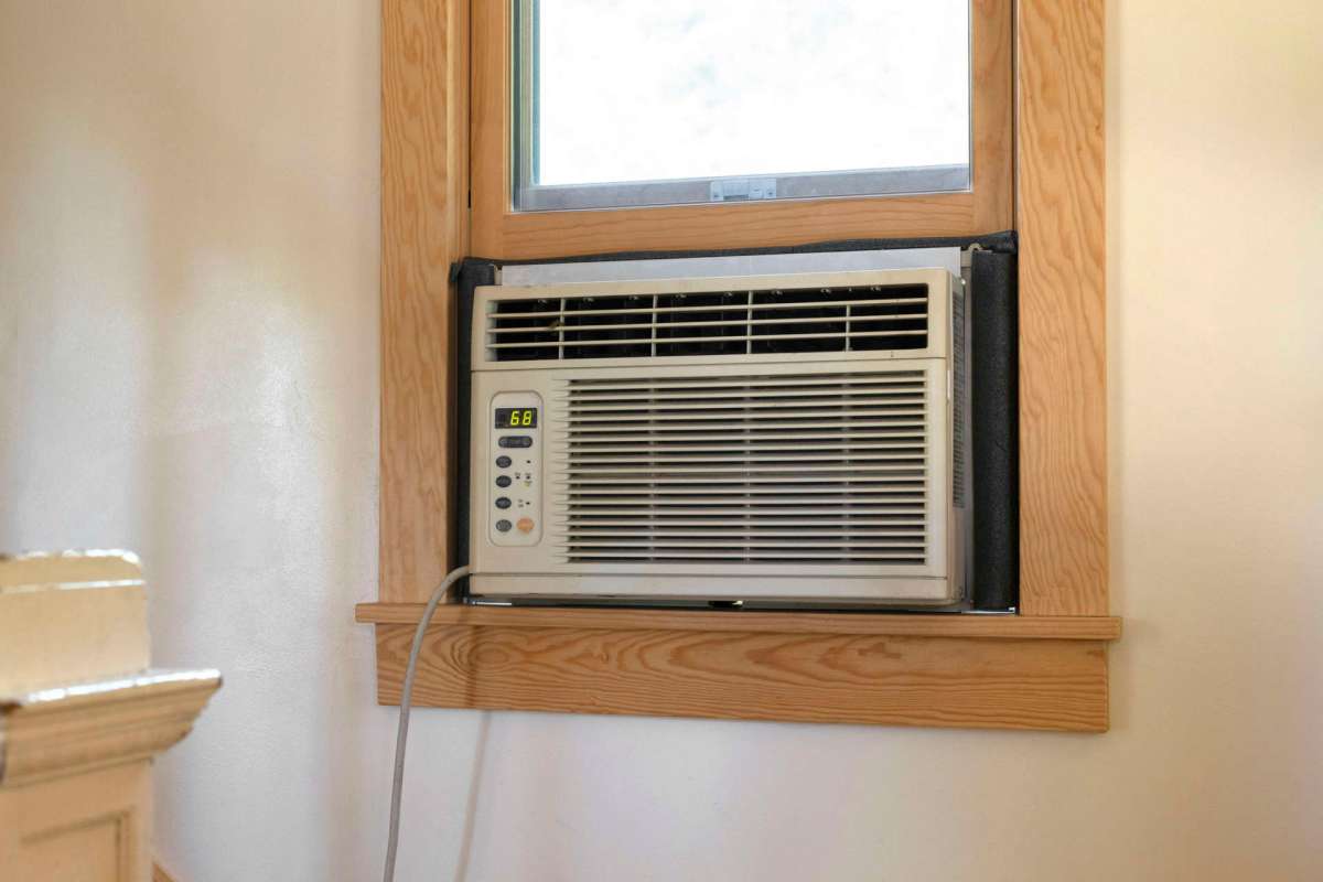 A window air conditioning unit installed next to a partially opened window.