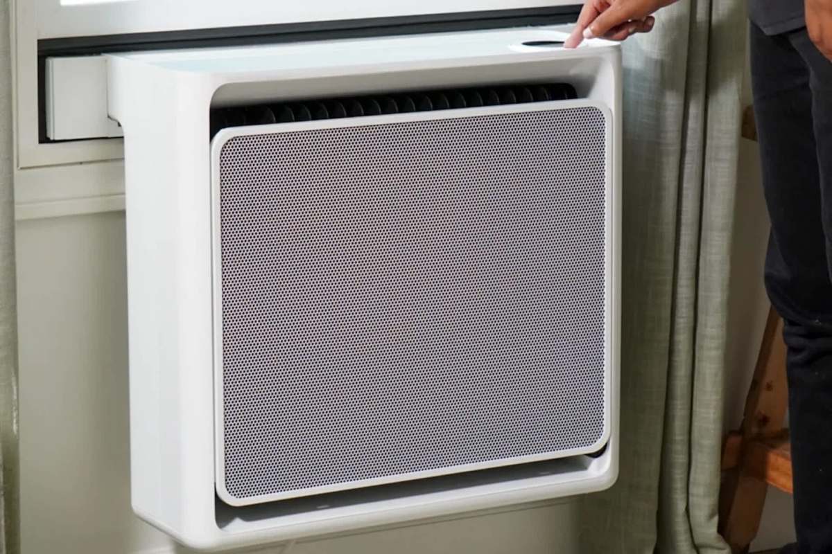 A person adjusts a window heat pump.