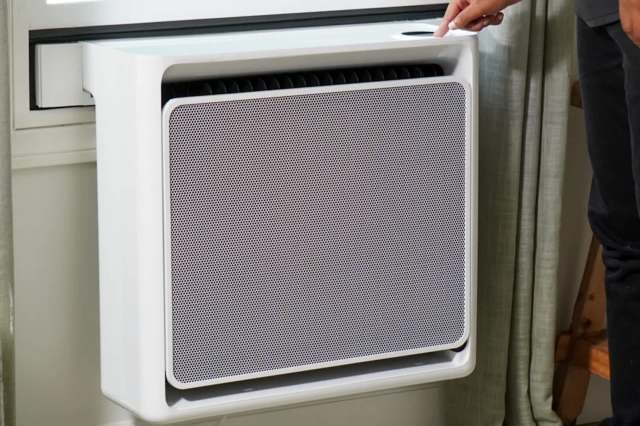 A person adjusts a window heat pump.