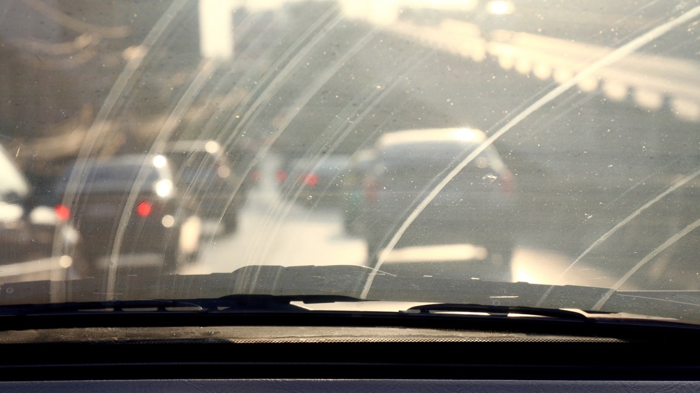 A view through a dirty windshield with cars on a road in the background.