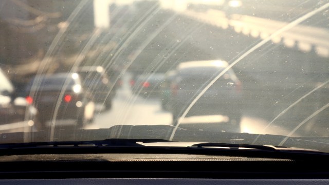 A view through a dirty windshield with cars on a road in the background.