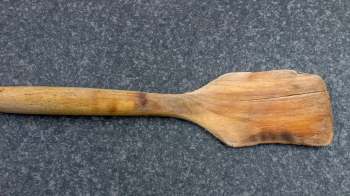 A wooden spatula with a crack on a dark textured surface.