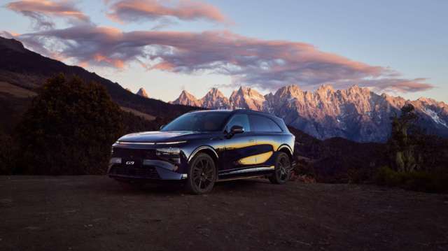 A black SUV parked on a dirt road with mountains and clouds in the background.