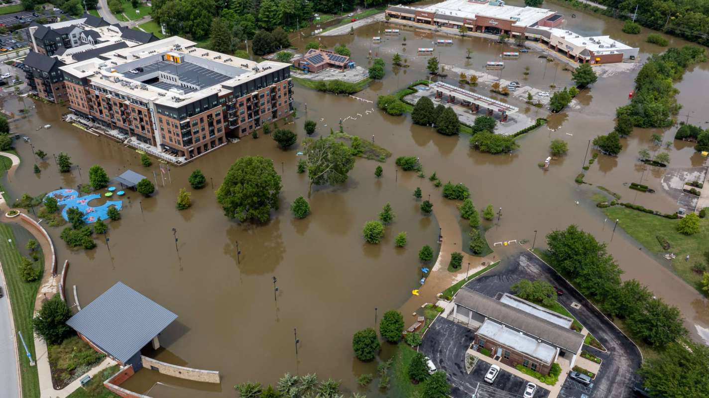 Aerial view of a flooded urban area with buildings, trees, and submerged playground equipment.