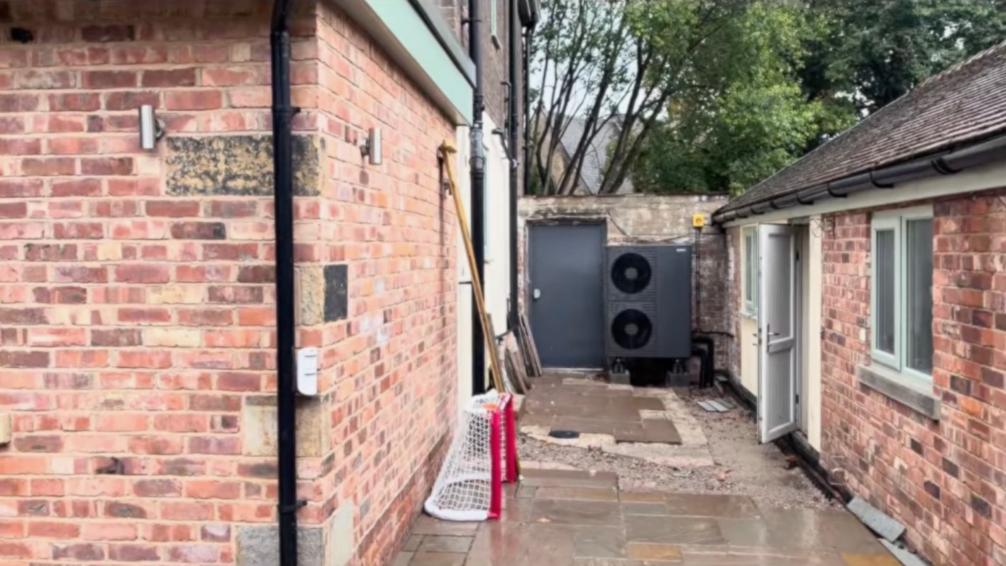 A narrow passageway between brick walls with an air conditioning unit and a small goal net.