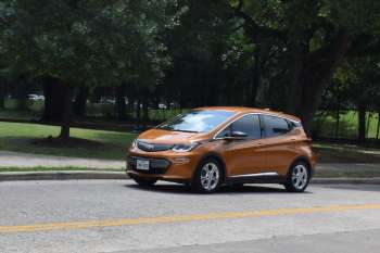 An orange electric car parked on the side of the street near a park.